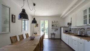 A spacious kitchen with a long wooden table, white cabinets, and hanging pendant lights.