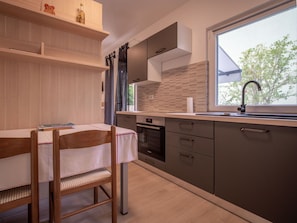 A modern kitchen with a dining area, featuring a window with a view of trees, a built-in oven, and a sink with a faucet.