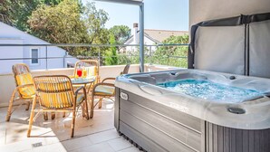 A balcony with a hot tub, wicker chairs, and a table with a drink.