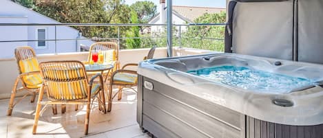 A balcony with a hot tub, wicker chairs, and a table with a drink.