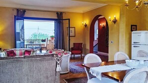 A living room with a sofa, dining table, and chairs. There is a window with curtains, a chandelier, and a refrigerator. - Wonderful  villa for 6 people with A/C, WIFI and terrace (Augusta)