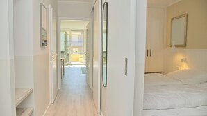 A hotel room with a bed, a bedside table, a mirror, and a door leading to another room.