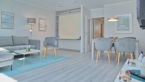A modern living room with a grey sofa, a coffee table, a dining table with chairs, and a wardrobe.