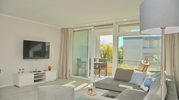 A modern living room with a sofa, TV, and a dining area visible through large glass doors.