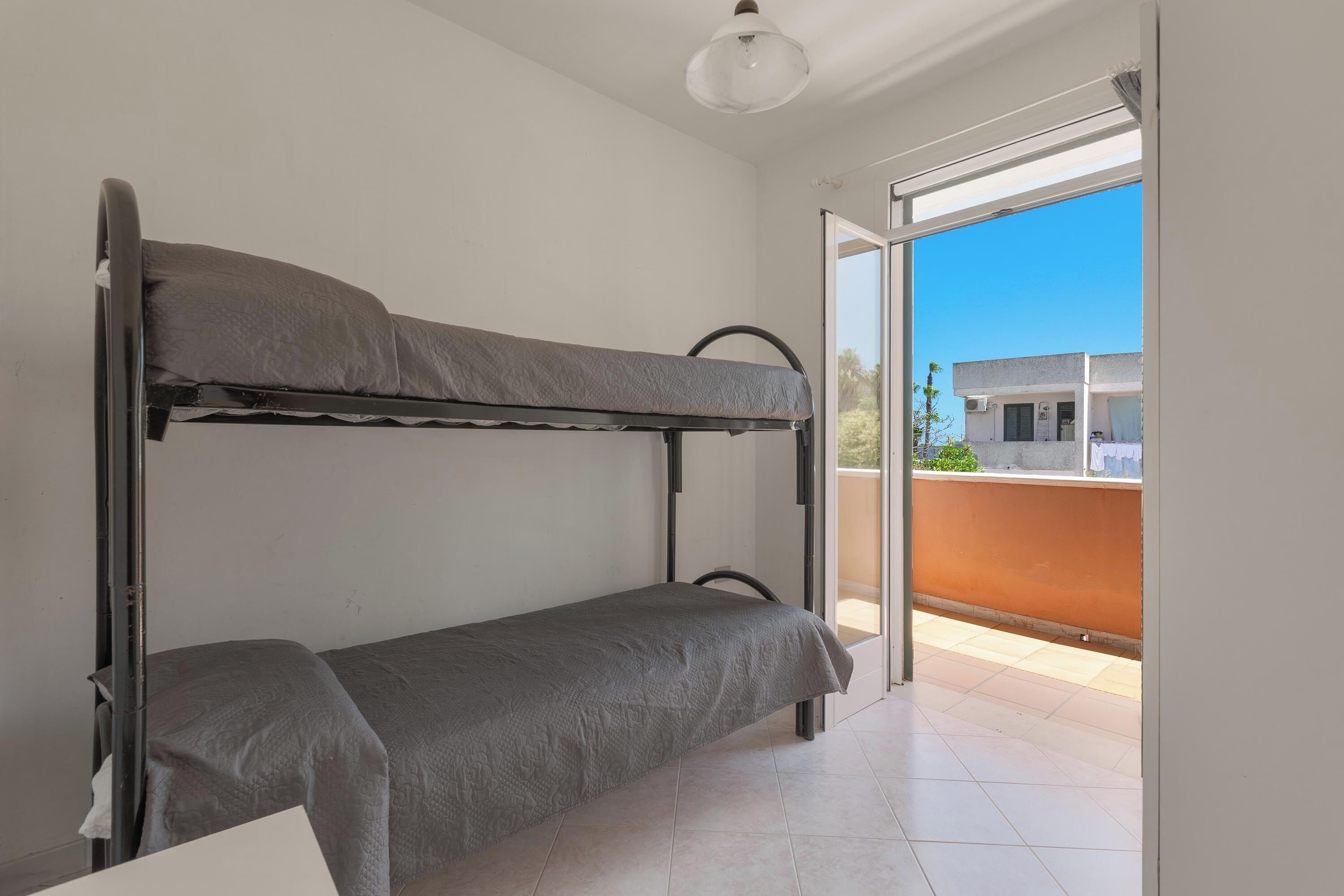 A bunk bed in a room with a view of a building through an open door.