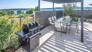 An outdoor patio with a grill, table, and chairs, overlooking a scenic lake. - Wonderful private villa for 8 guests with A/C, private pool, WIFI, TV, terrace and pets allowed (Medulin)