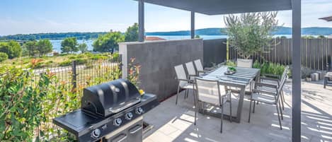 Une terrasse extérieure équipée d’un barbecue, d’une table et de chaises, avec vue sur un magnifique lac.