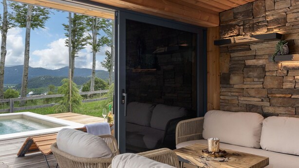 Une chambre moderne avec un mur en pierre, un plafond en bois et une vue sur les montagnes. On y trouve un canapé, une table et une chaise.