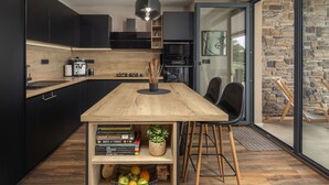 Une cuisine moderne avec des meubles de couleur sombre, une table en bois et une bibliothèque intégrée.