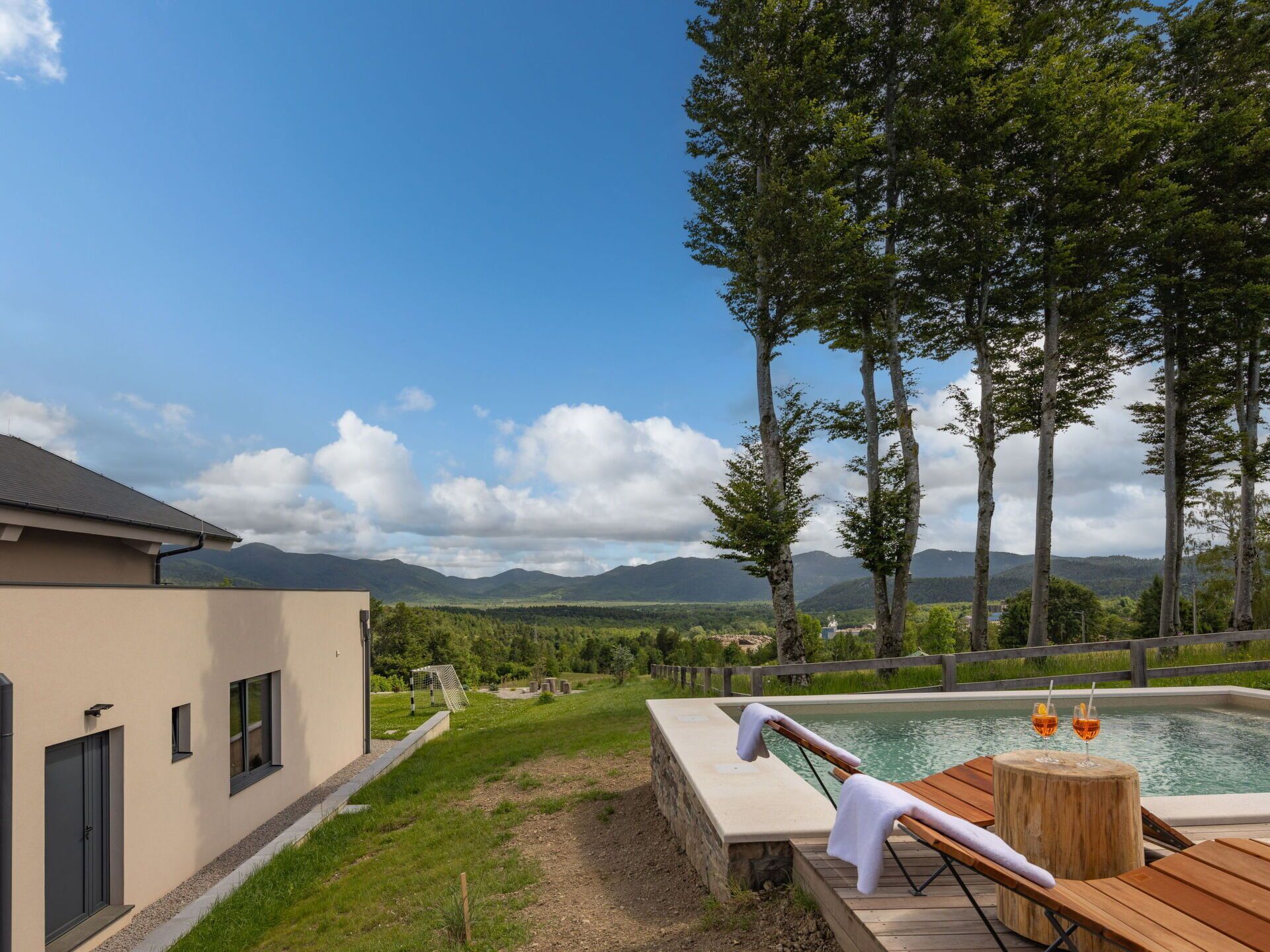 A modern building with a swimming pool, lounge chairs, and a view of mountains.