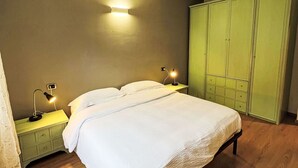 A neatly made bed in a room with wooden flooring, two bedside tables with lamps, and a green wardrobe. - Cosy apartment for 4 people with WIFI, TV, patio and pets allowed (Pieve Di Ledro)