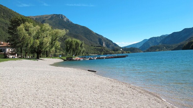 A pebble beach with boats docked, a house on the left, and mountains in the background. - Cosy apartment for 4 people with WIFI, TV, patio and pets allowed (Pieve Di Ledro)