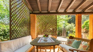 A covered patio with a wooden table, white cushioned seating, and a lattice backdrop.