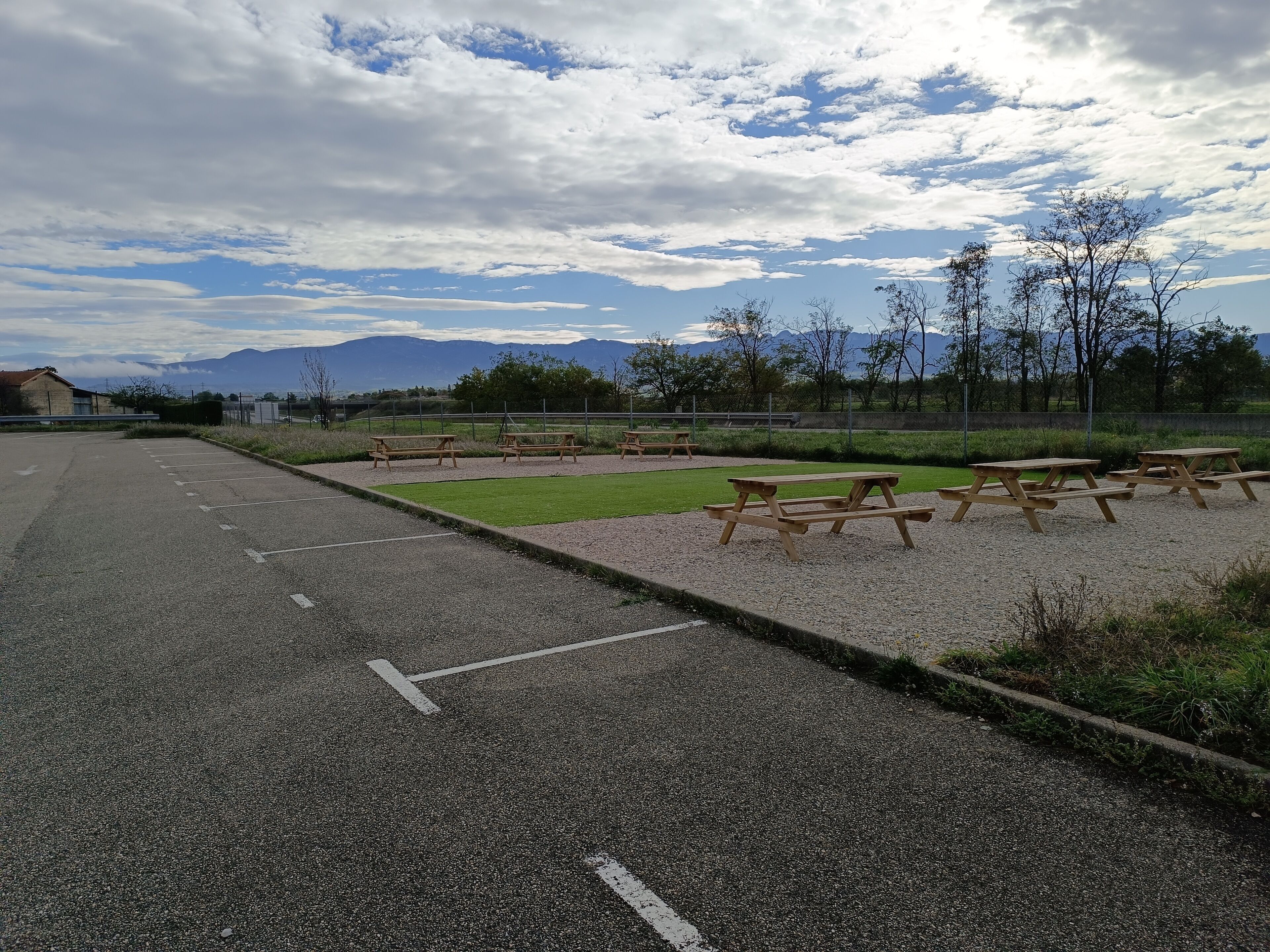 Un espacio para estacionar con mesas de picnic y un campo cubierto de césped.