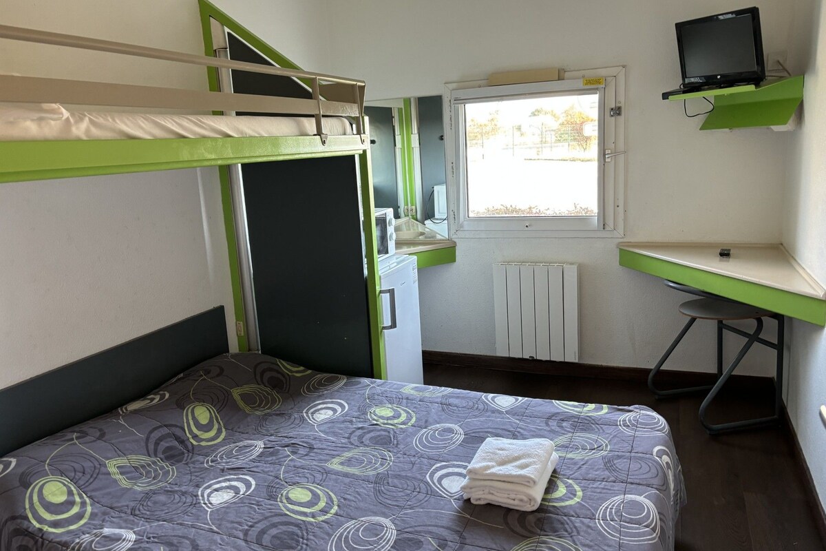 Ett studentrum med våningssängar, ett skrivbord, en dator och ett fönster med utsikt över träd.