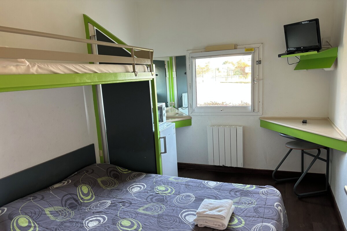 A dormitory room with bunk beds, a desk, a computer, and a window with a view.
