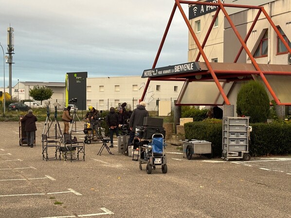 A hotel entrance with a signboard, a metal structure, and a parking area with equipment. - HOTEL PARIS VALENCE (Bourg-de-Peage)