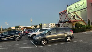 A hotel parking lot with several cars parked, a building with a sign reading "HOTEL Paris Valence," and a red metal structure.