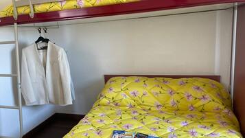 Een stapelbed met een gele bloemenbeddover en een wit jasje dat aan een metalen rek hangt.