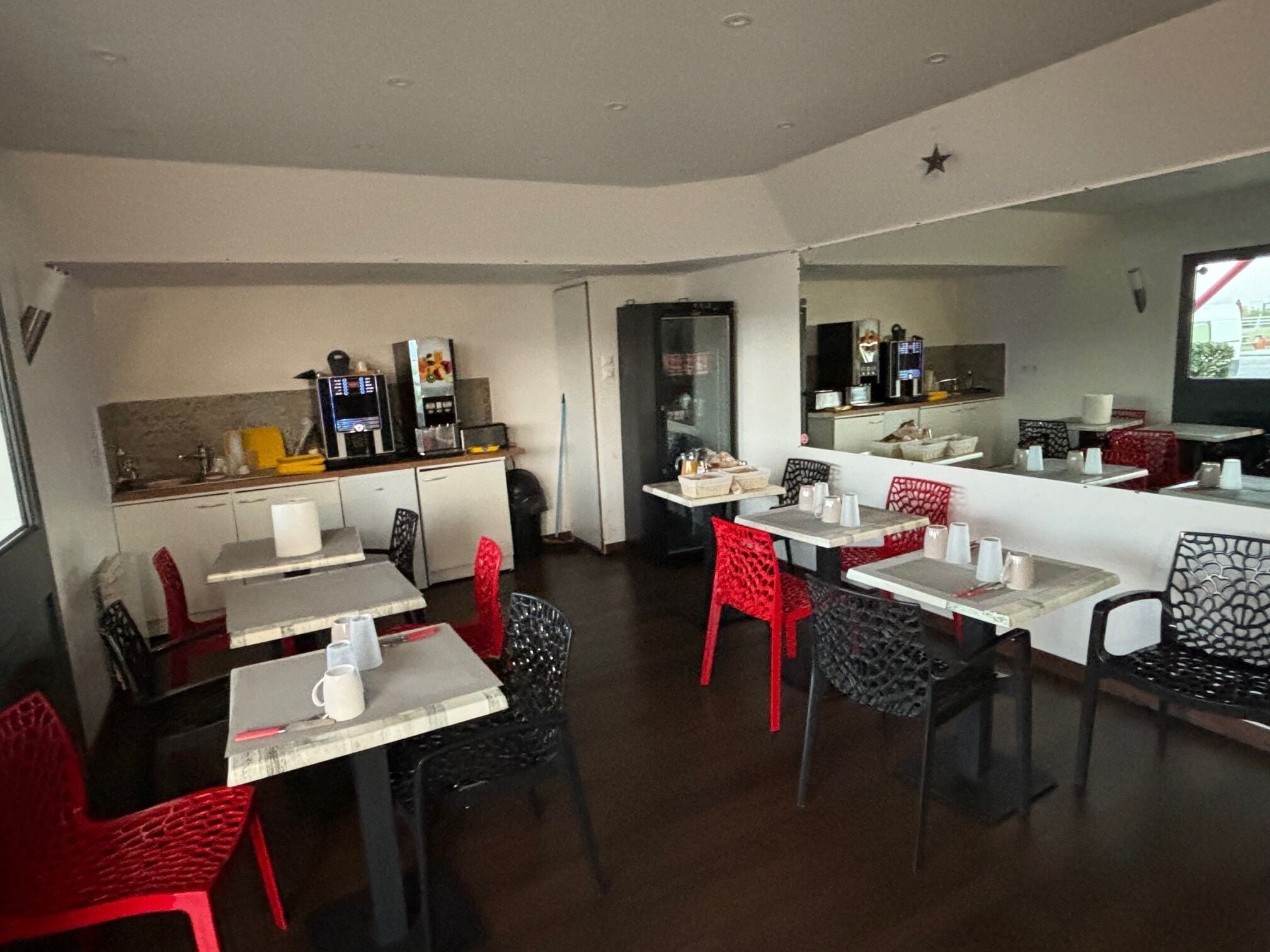 Een restaurant met tafels en stoelen, een toonbank met een koffieapparaat en een keukenhoek.