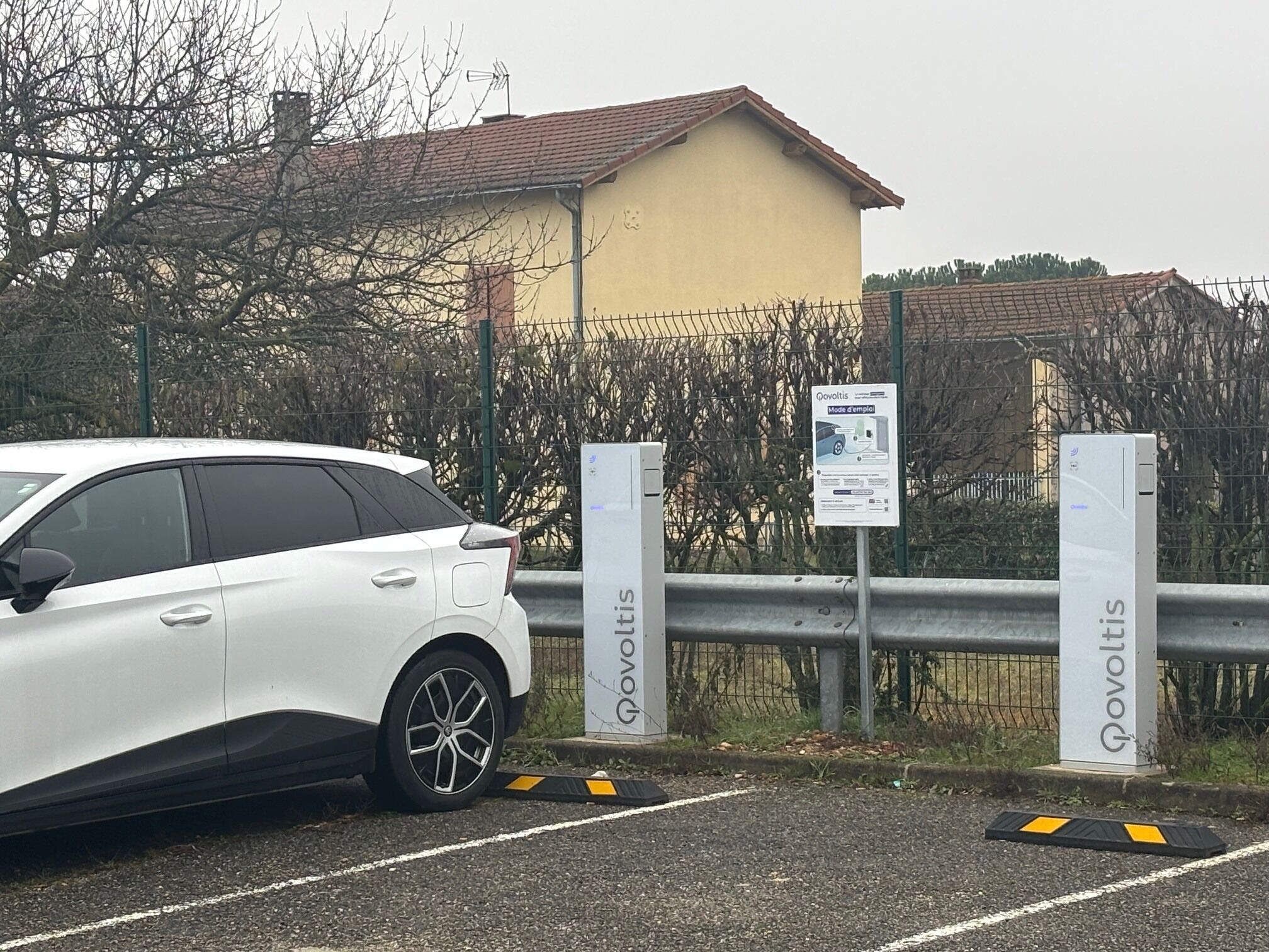 A white car parked near a gated area with a building in the background.