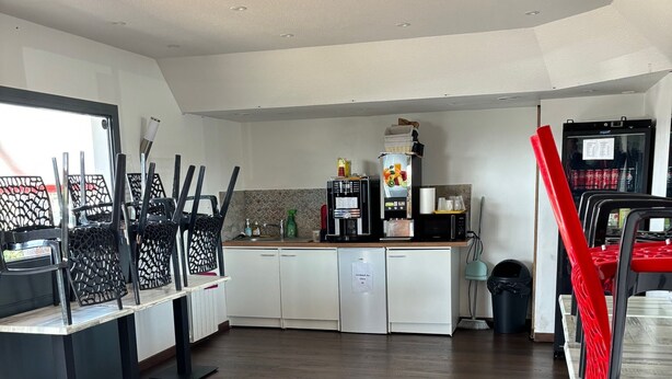 A spacious room with a kitchen area, including a refrigerator, coffee machine, and a sink.