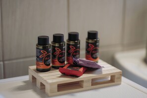 Un vassoio di legno con quattro flaconi di gel doccia all'oliva e uno spazzolino da denti rosso.
