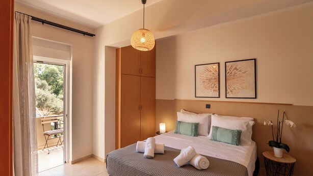 A bedroom with a bed, a nightstand, a hanging light fixture, a window with curtains, and a view of the outside.