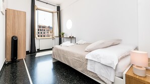 Ein modernes Schlafzimmer mit Bett, Nachttisch und einem Fenster mit Blick auf Gebäude.