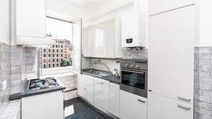 Eine moderne Küche mit weißen Schränken, einem Gasherd, einem Backofen und einem Fenster mit Blick auf die Stadt.