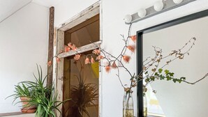 Un baño con ventana, espejo, planta en maceta y dispensador de jabón.