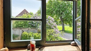 Una ventana con una vela en el alféizar, con vista a un jardín con árboles y una valla de madera.