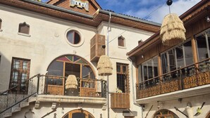 Un bâtiment traditionnel doté d’un balcon en bois, de grandes fenêtres en arc de cercle et d’une enseigne sur laquelle on peut lire « KONAGL ».