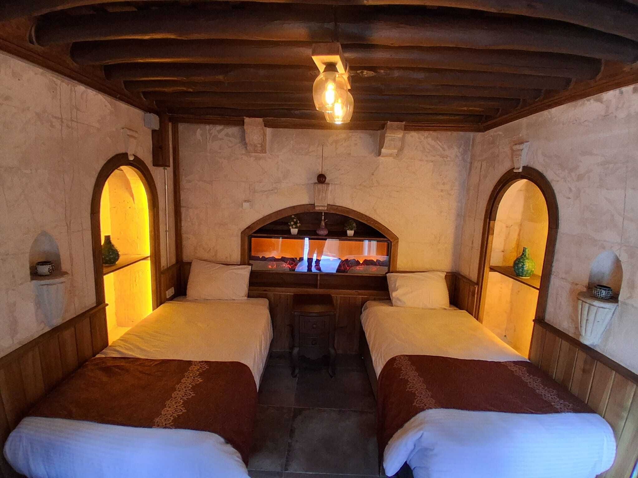 Une chambre rustique avec deux lits, un mur en pierre, des poutres en bois et une cheminée en pierre.