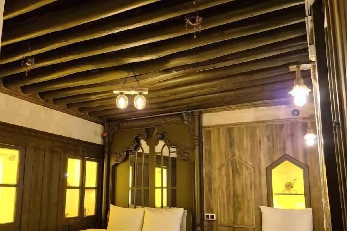 Quarto com duas camas, paredes de madeira e teto inclinado com vigas aparentes.