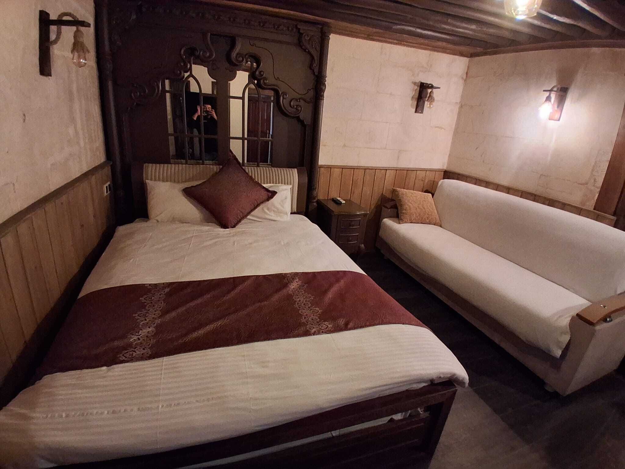 Een slaapkamer met een groot bed, een kleinere bank, een nachtkastje en een spiegel.