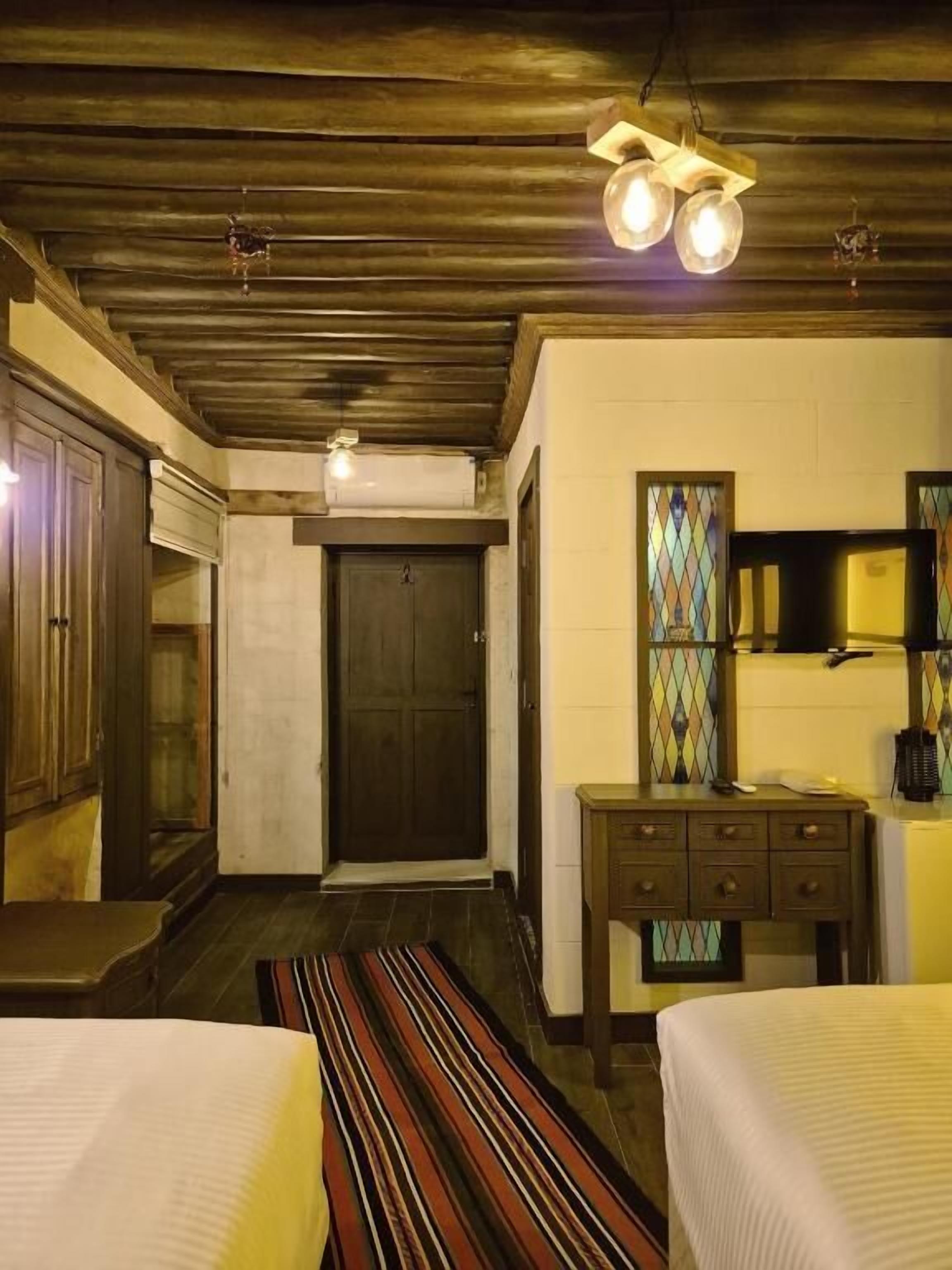A room with two beds, a wooden ceiling, a small table, and a mirror.