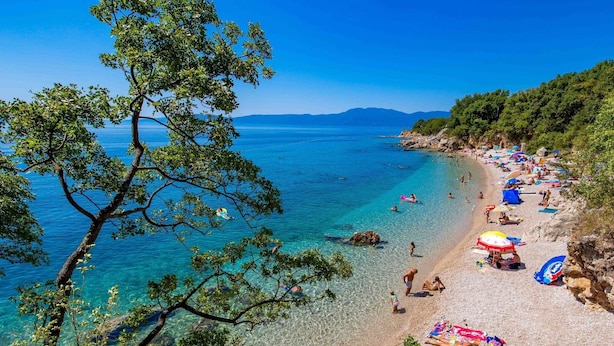Uma praia com águas cristalinas, pessoas tomando sol e guarda-sóis.
