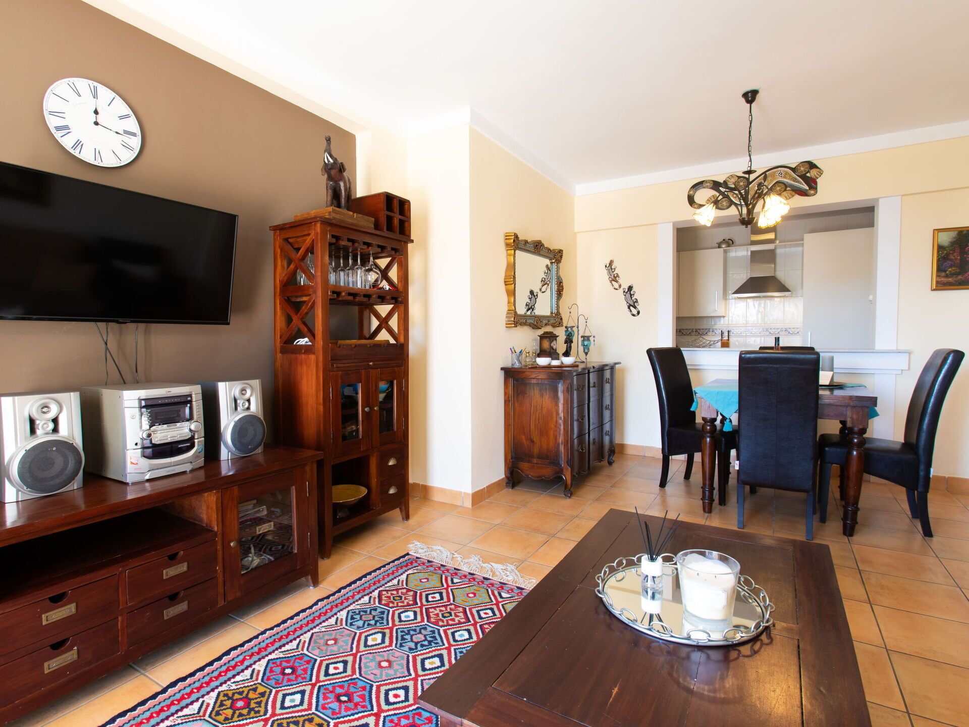 A living room with a TV, speakers, a wooden cabinet, and a dining area with chairs and a table.