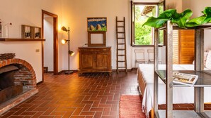 A rustic room with a brick fireplace, wooden ceiling beams, a wooden cabinet, a ladder, and a window with a view of greenery. - Cosy apartment for 4 guests with WIFI and patio (Gravedona)