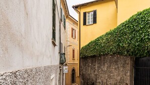 A narrow alleyway with a yellow building on the right, a stone wall, and a black gate. - Cosy apartment for 3 guests with WIFI and patio (Gravedona)