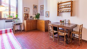 A cozy kitchen with wooden cabinets, a dining table with chairs, and a window with flowers. - Cosy apartment for 3 guests with WIFI and patio (Gravedona)