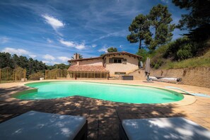 Relax by the oval-shaped pool surrounded by a lush garden and a traditional building.