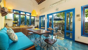 A cozy dining area with a blue sofa, a wooden table, and chairs. There is a yellow pendant light above the table. - Loft House 2BR Seaside An Bang Beach (Da Nang)