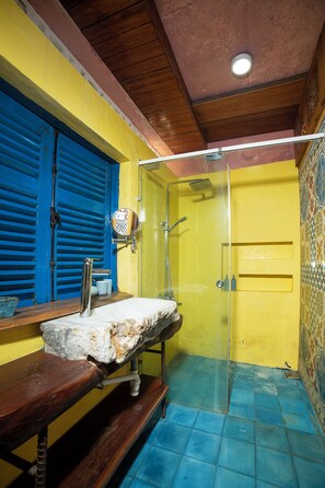 A bathroom with a wooden bench, a sink with a mirror, a shower with a glass door, and a yellow wall. - Loft House 2BR Seaside An Bang Beach (Da Nang)