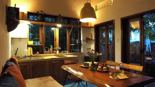 A cozy kitchen with wooden cabinets, a large window, and a dining table set for two. - Loft House 2BR Seaside An Bang Beach (Da Nang)