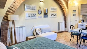 A cozy bedroom with a brick arch, a bed, a desk, and a radiator.