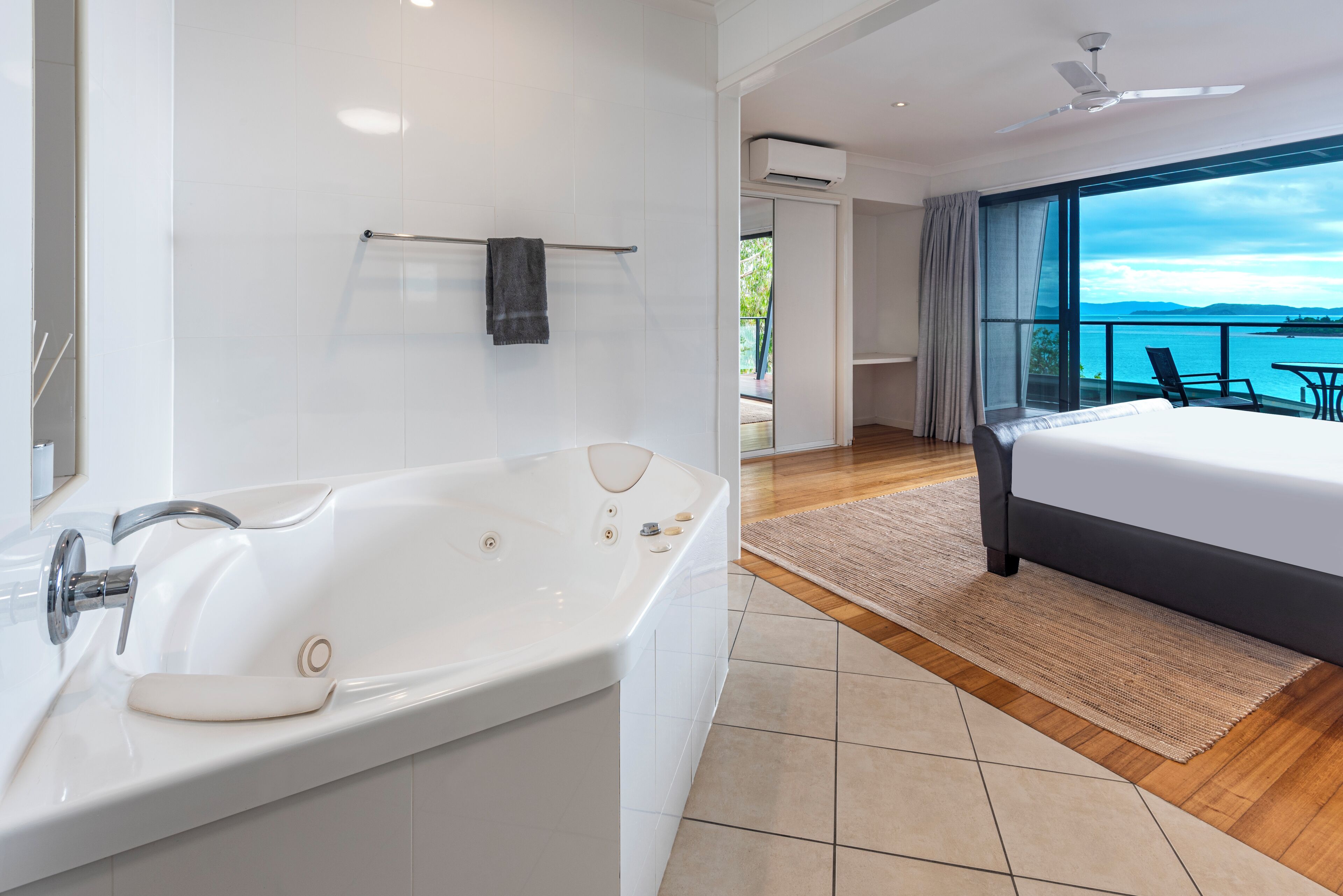 A modern hotel room with a large bathtub, a bed, and a balcony with a view of the sea.