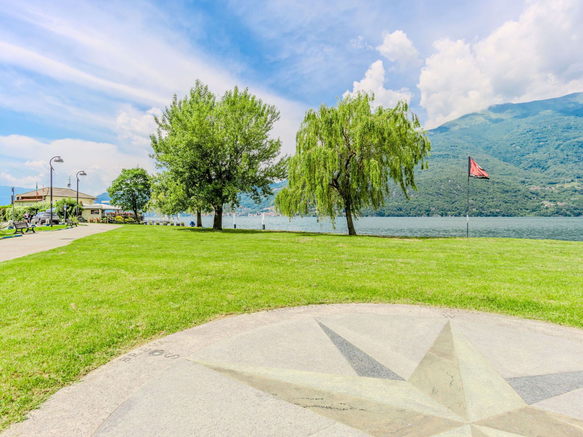 A park with a paved area, trees, a lake, and a mountain in the background.