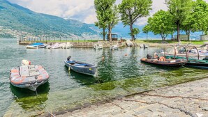 A lakeside dock with several boats, a stone pier, and a mountainous backdrop.